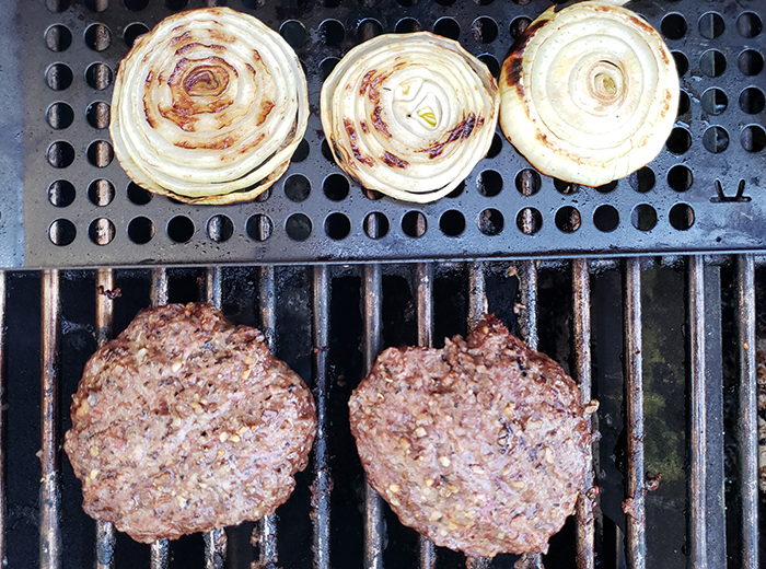 three onion slices and two burgers cooking on a grill
