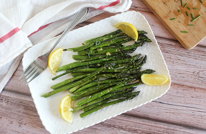 overhead view of roasted asparagus on a white plate with lemon wedges