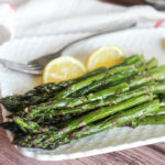 a close up of roasted asparagus spears on white plate with lemon wedges