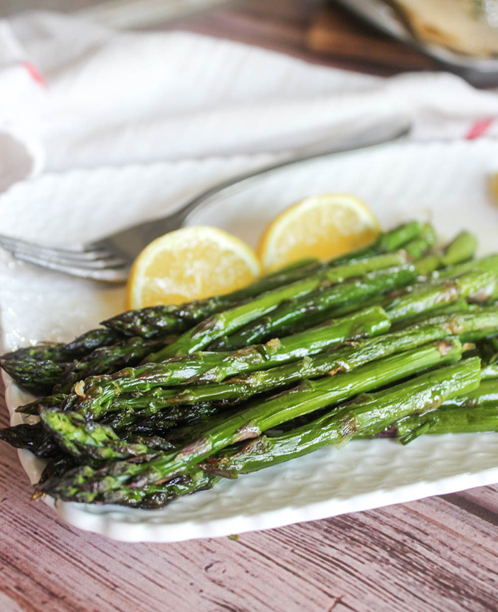 a close up of roasted asparagus spears on white plate with lemon wedges