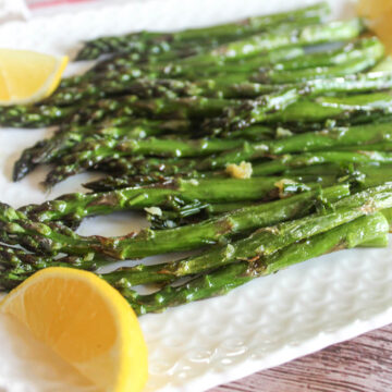A close up of roasted asparagus on a white plate with lemon wedges