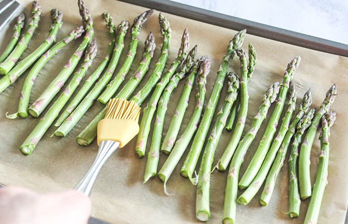 brushing oil onto raw asparagus with a basting brush