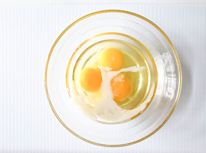 three cracked eggs in a bowl with milk