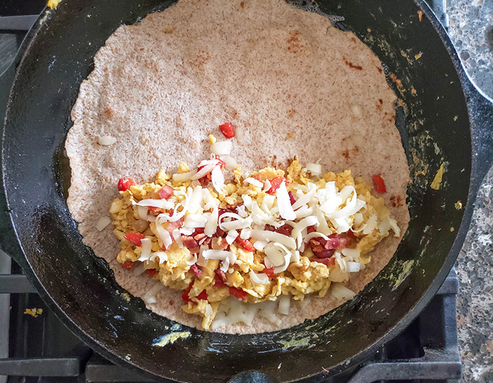 tortilla topped with eggs, peppers, bagon and cheese in a skillet