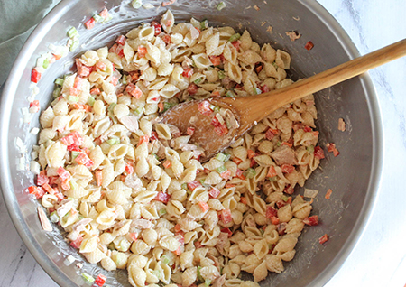 wooden spoon and tuna salad incredients in bowl mixing together
