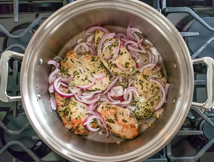 a view of chicken cooking in a pan with onions