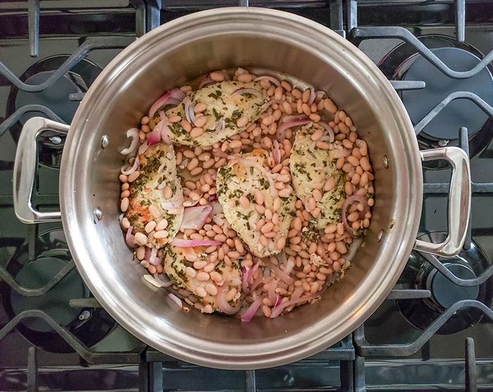 overhead of chicken cooking in a pan with beans