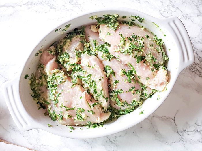 an overhead view of boneless chicken breasts covered in herb marinade