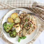 An overhead view of garlic herb chicken with white beans on a plate with broccoli and cauliflower