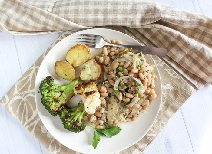 An overhead view of garlic herb chicken with white beans on a plate with broccoli and cauliflower