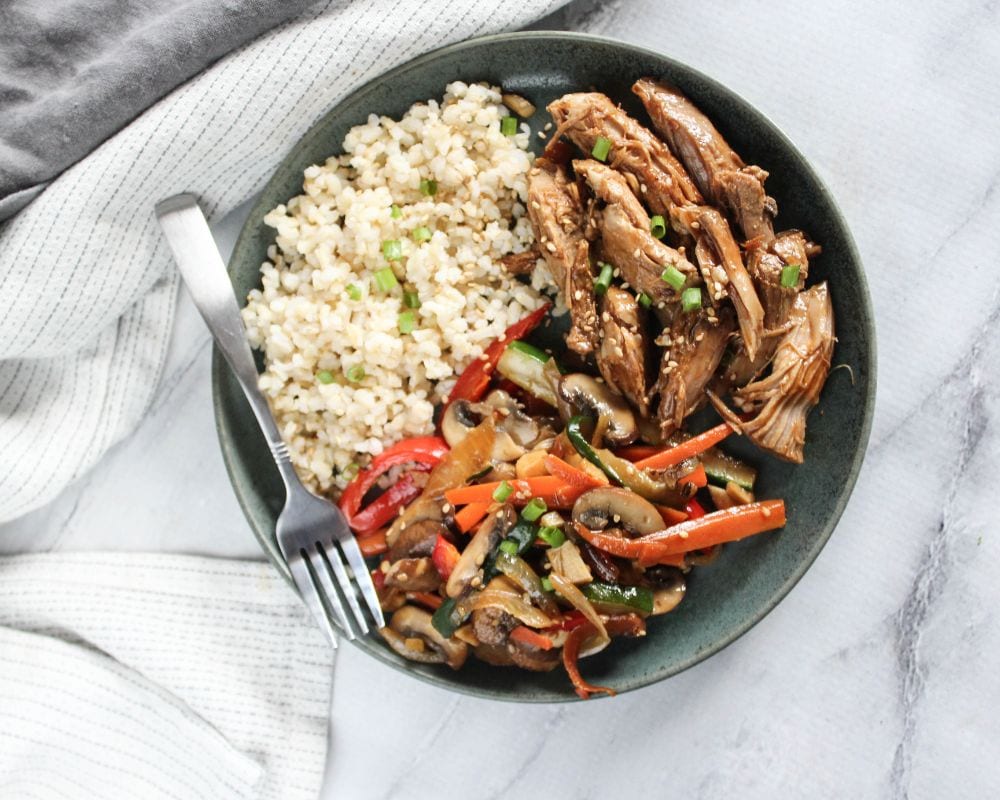 an overhead shot of slow cooker asian pork on a plate with stir fried vegetables and rice