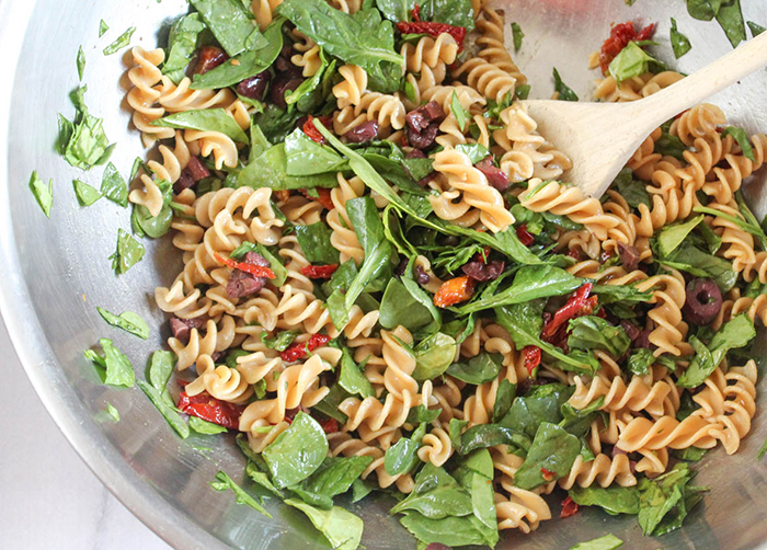 Spinach pasta salad all mixed together in a mixing bowl.