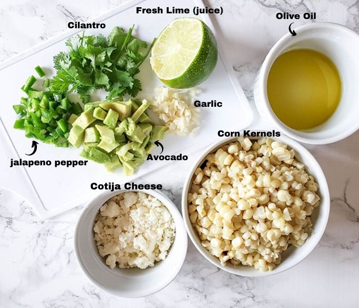 the ingredients for corn salad, cotja cheese, diced avocado, jalapeno pepper, cilantro, lime juice, olive oil garlic and corn kernels