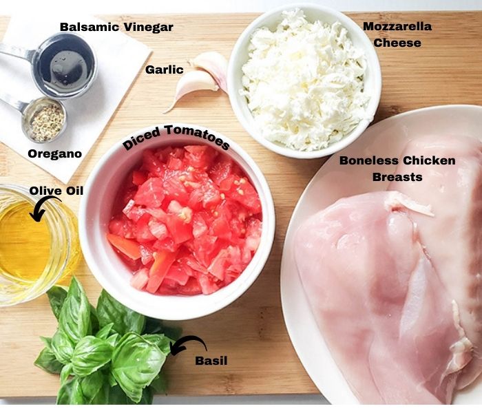 an overhead shot of the ingredients for grilled chicken parmesan: basil, oil, oregano, tomatoes, chicken and tomatoes