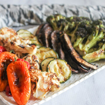 A close up picture of grilled peppers, cauliflower, zucchini, mushrooms and broccoli on a platter