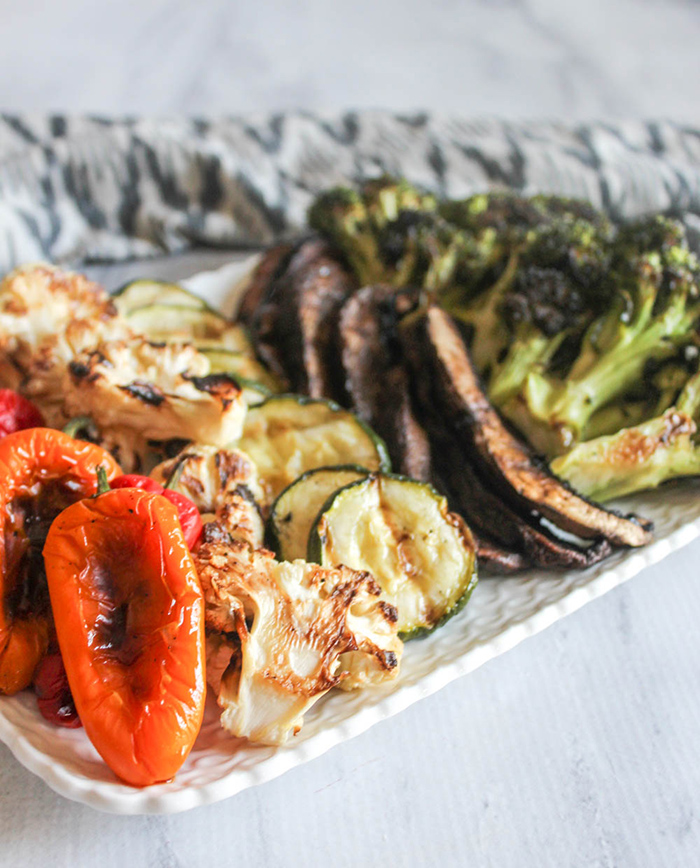 A close up picture of grilled peppers, cauliflower, zucchini, mushrooms and broccoli on a platter