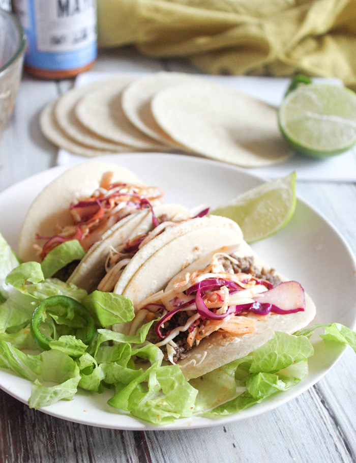 three korean tacos on a plate with lettuce