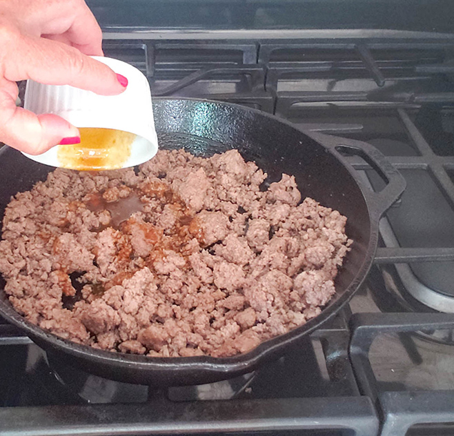 ground beef in a skillet with sauce pouring into it.