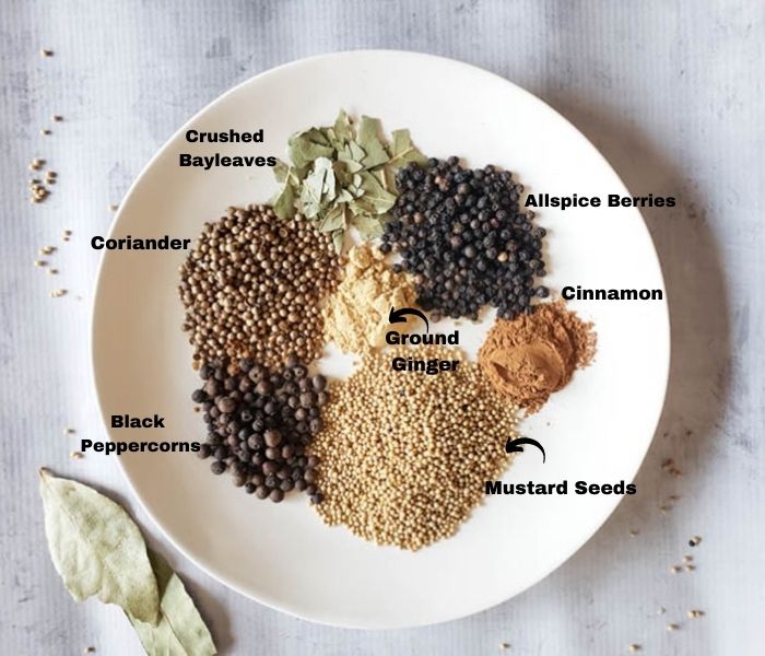 a picture of the pickle spice ingredients on a plate: mustard seeds, peppercorns, coriander, ginger, cinnamon, crushed bayleaves on a plate