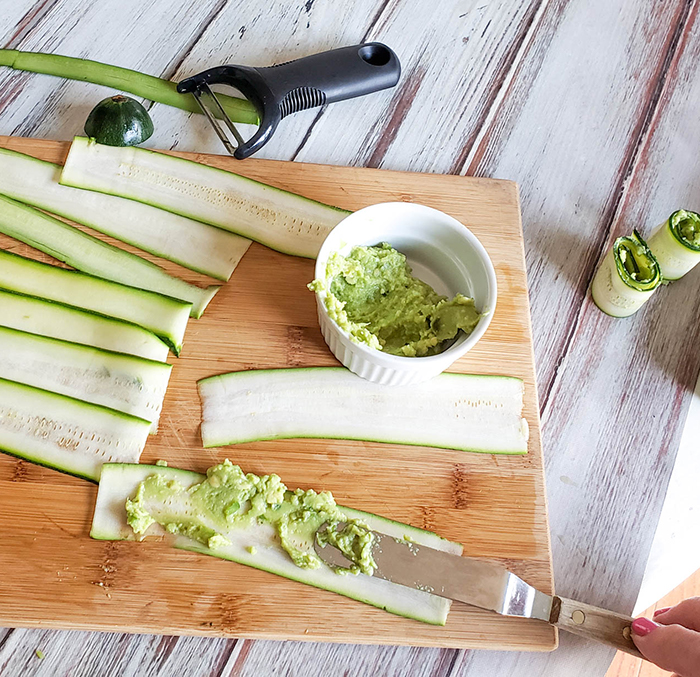 a picture of a offset spatula spreading guacamole onto a zucchini strip