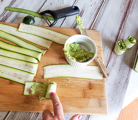 This photo shows step three of the recipe. Zucchini ribbons are rolled up using hands after covering with guacamole. 