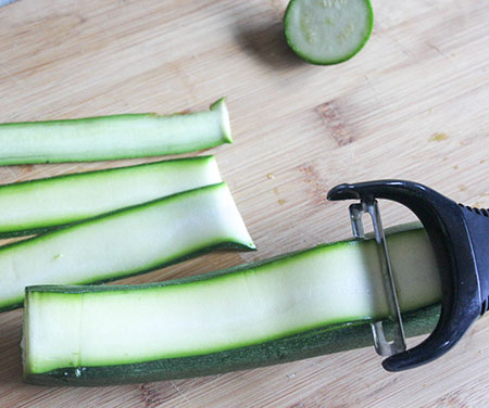 a vegetable peeler peeling the zucchini into strips