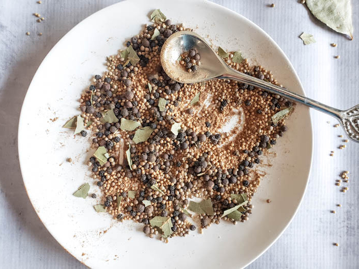 All of the pickle spice ingredients mixed together on a white plate with a spoon