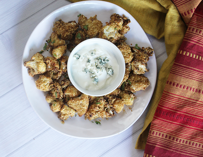 an overhead view of air fried cauliflower bites on a white dish with a bowl of blue cheese dip
