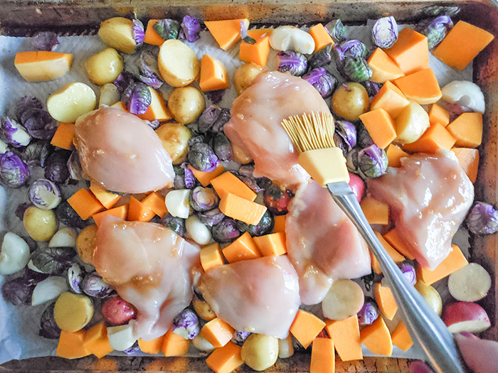 an overhead of the chicken and vegetables uncooked on a sheet pan basting