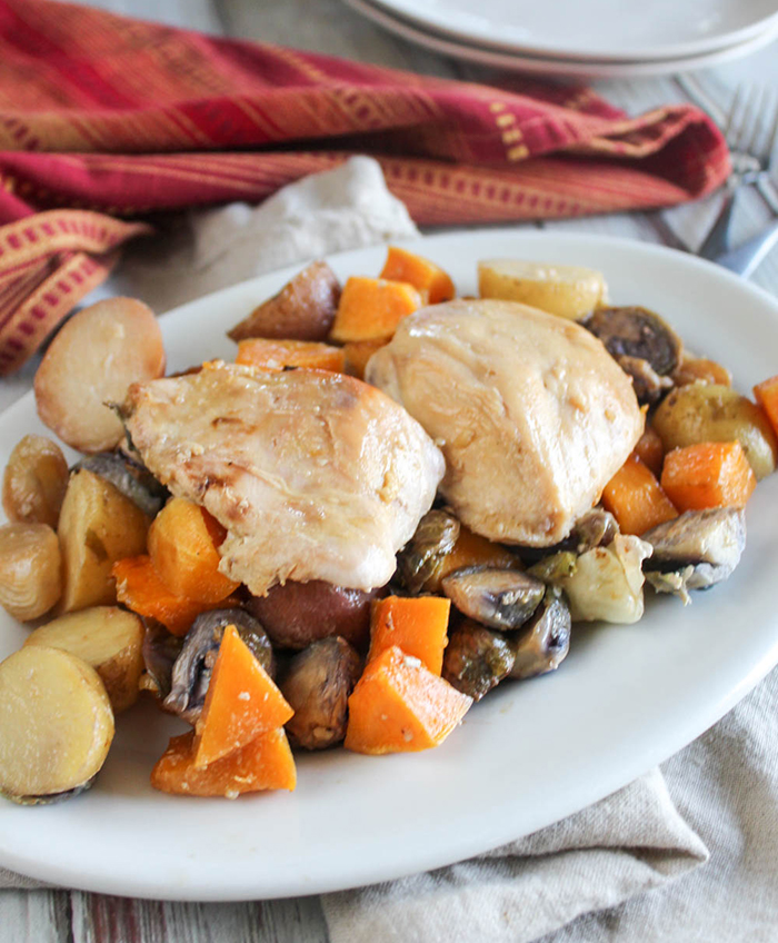 two chicken breasts on top of roasted vegetables on a white platter