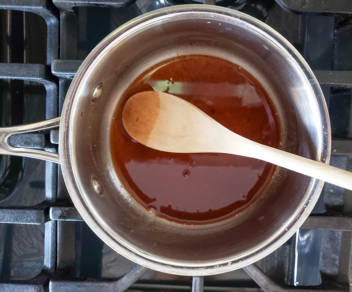 An overhead view of the syrup mixture in a saucepan with a spoon.