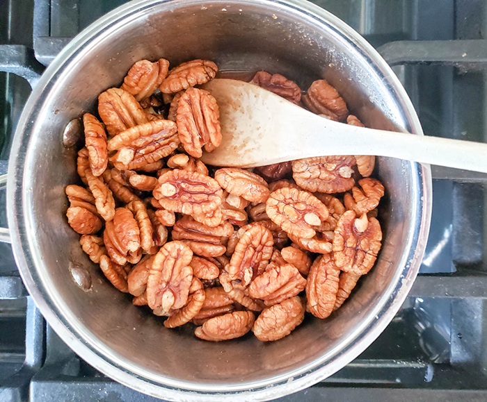 An overhead view of pecans in a saucepan with a spoon.