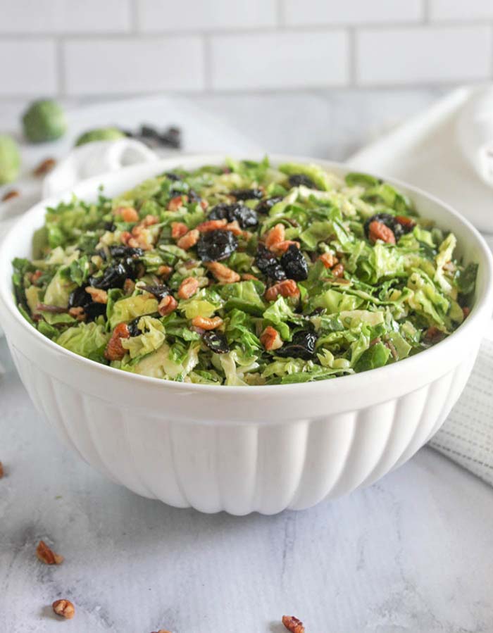 a close up picture of the kale and brussels sprouts salad in a white bowl