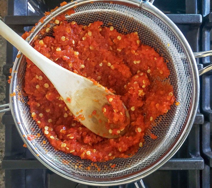 pureed jalapeno mixture in a strainer over a pot with a wooden spoon