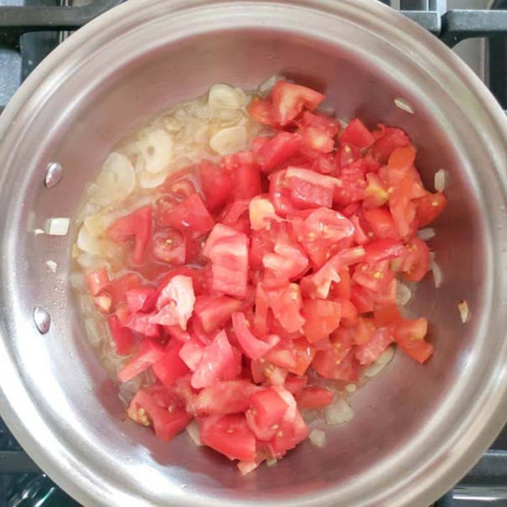 a picture of tomatoes added to a pan with garlic and onions for process step 3