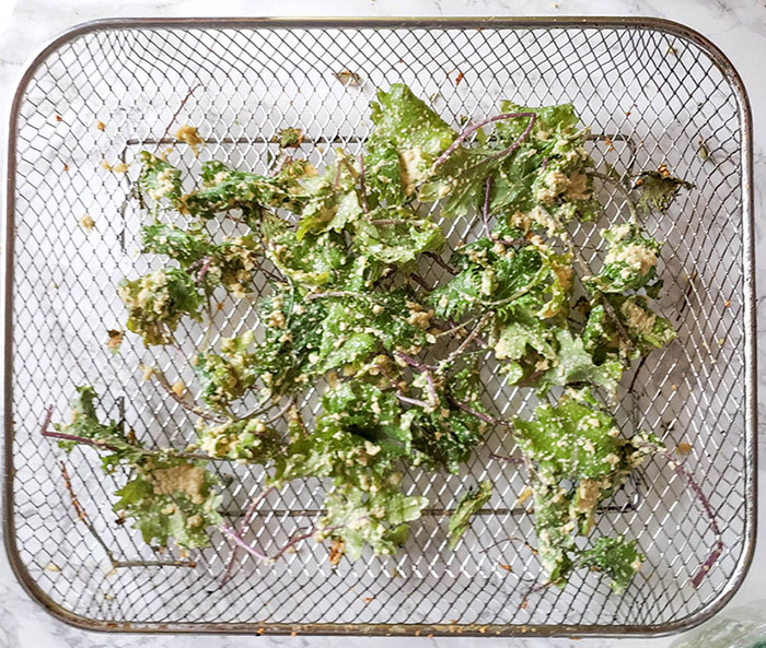 coated kale leaves on an air fryer tray