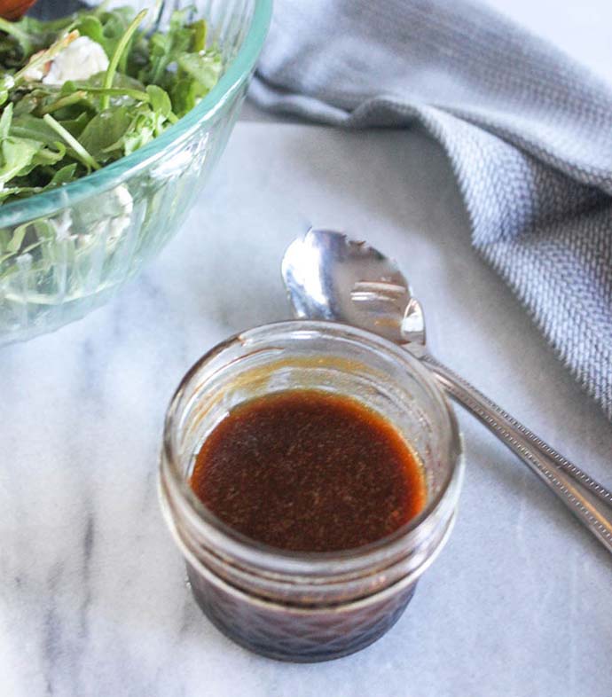 salad dressing in a jar with a bowl of salad in the backgroudn