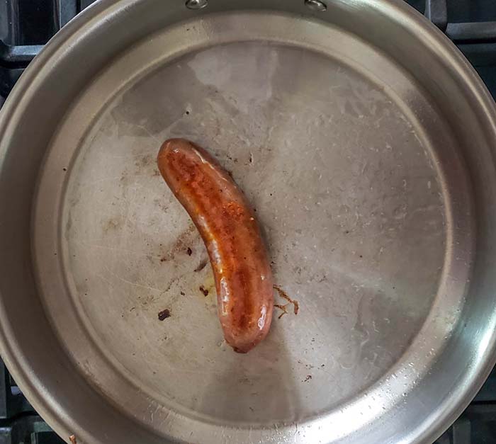 a sausage link cooking in a skillet