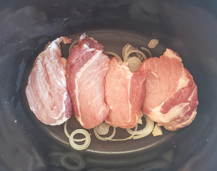 raw pork chops in a crock pot on top of onions