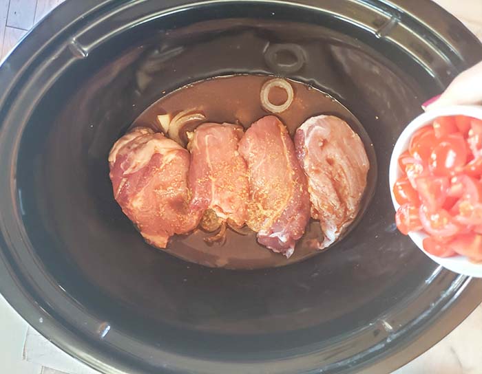 pork chops in a slow cooker with tomatoes pouring over it.