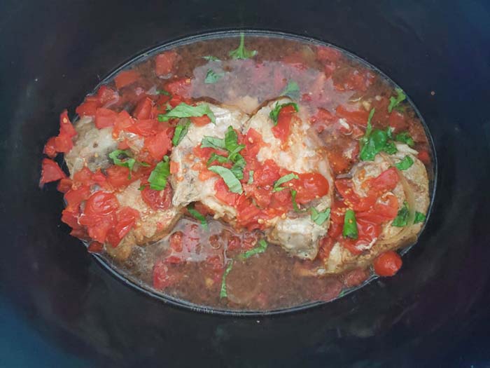 cooked pork in the slow cooker with fresh basil on top.