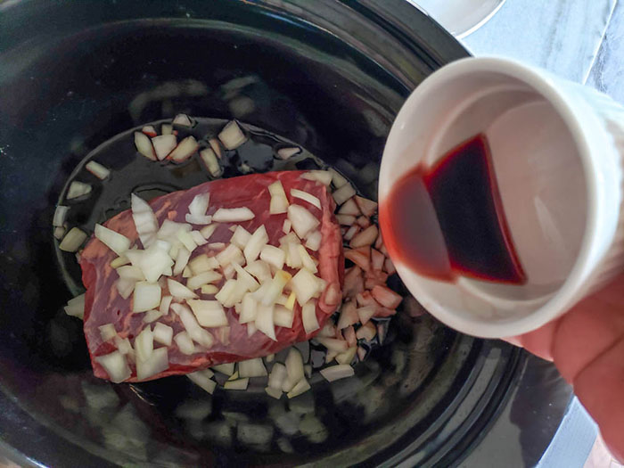 tri tip roast in pot with onions and wine pouring in