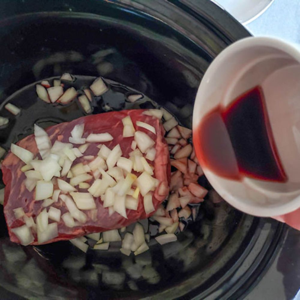 Process step 1 tri tip roast in a slow cooker with onions and red wine pouring in