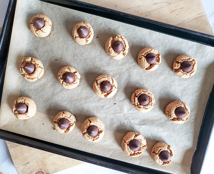 Step six of recipe with baked cookies out of oven to demonstrate chocolate kiss placed in center of cookie.