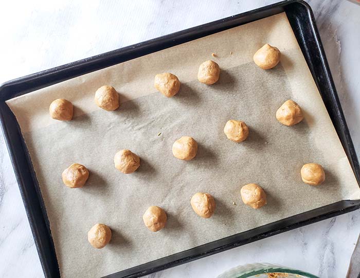 One inch shaped cookie dough balls in three rows on metal cookie sheet lined with parchment paper showing step 5.