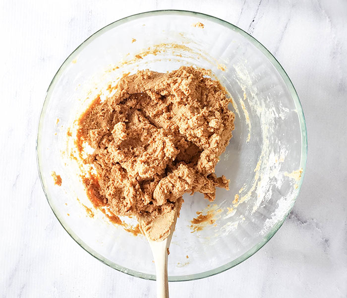 Overhead image showing mixing dry ingredients into wet to form dough with wooden spoon.