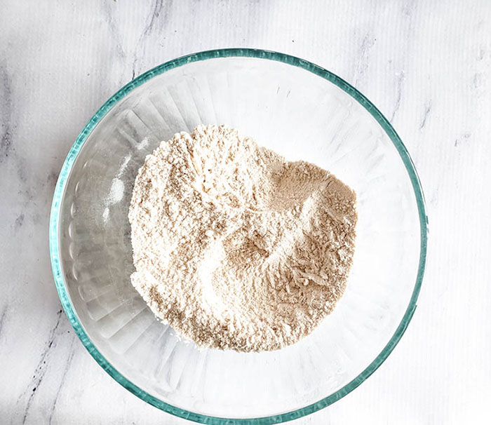 Glass mixing bowl holding flour, salt and baking soda to show step two of recipe with mixing these three ingredients together.