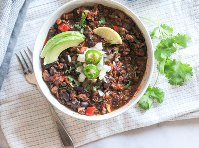 an overhead view of beef chili with jalapeno and avocado slices with cilantro on the side