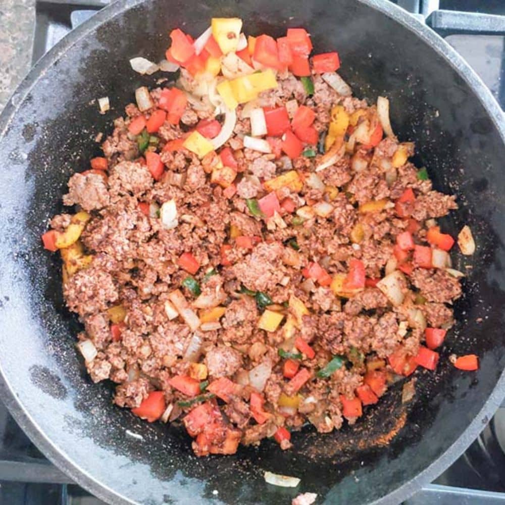 beer crockpot chili step 3 beef, peppers and onions cooking in a skillet with seasonings added