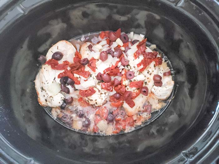 Slow cooker Mediterranean chicken cooking in slow cooker with oregano, sun-dried tomatoes, garlic and onions